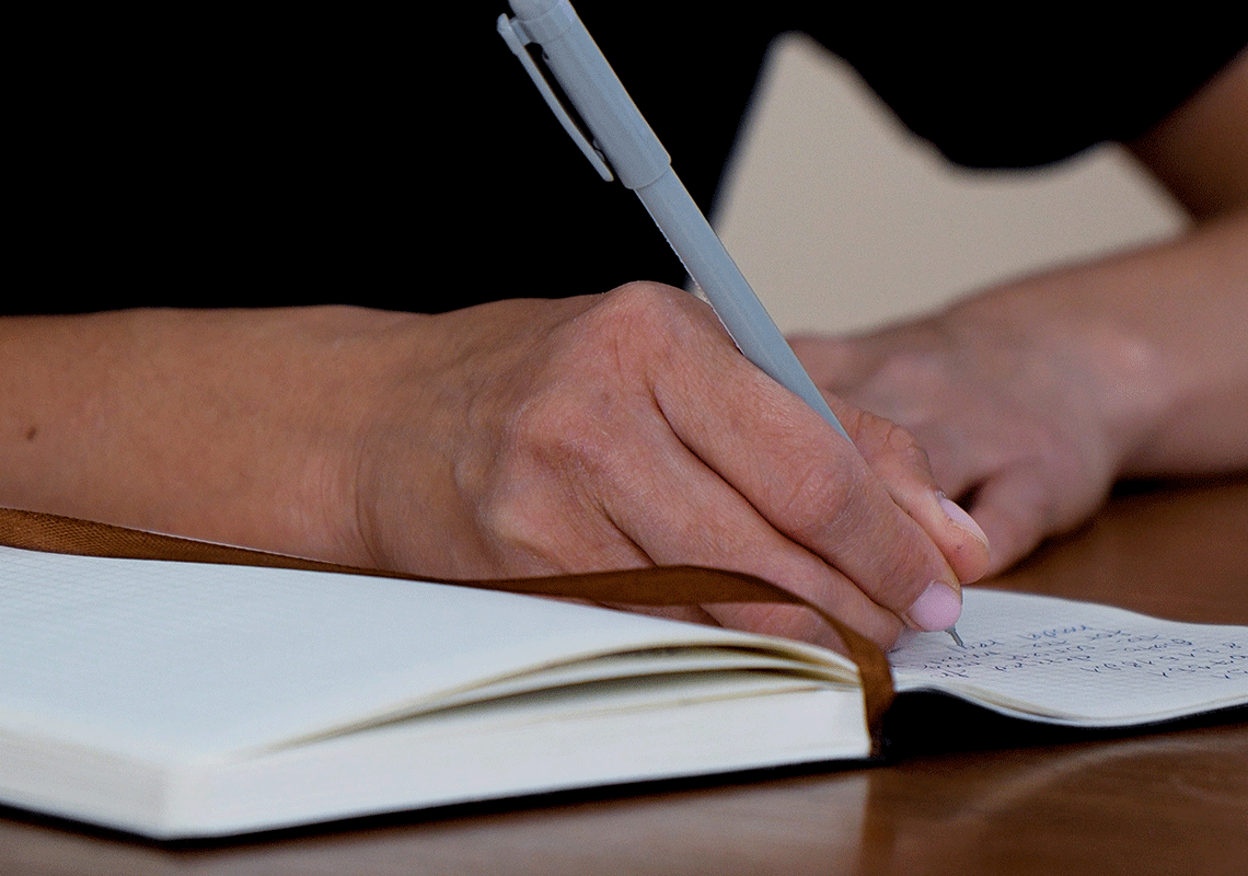 Persona che scrive, primo piano sulle mani, la penna e il quaderno